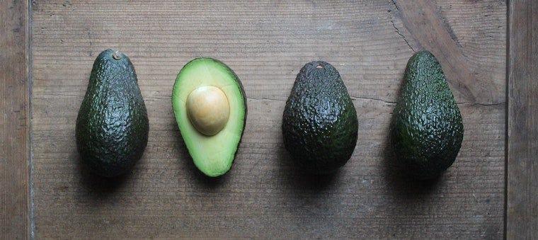 Drie hele avocado's en een half gesneden avocado op een houten snijplank - kunnen katten avocado eten?