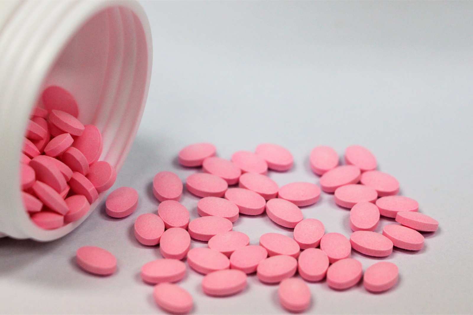 Roze tabletten van prednisolon gemorst uit witte plastic fles op witte achtergrond.