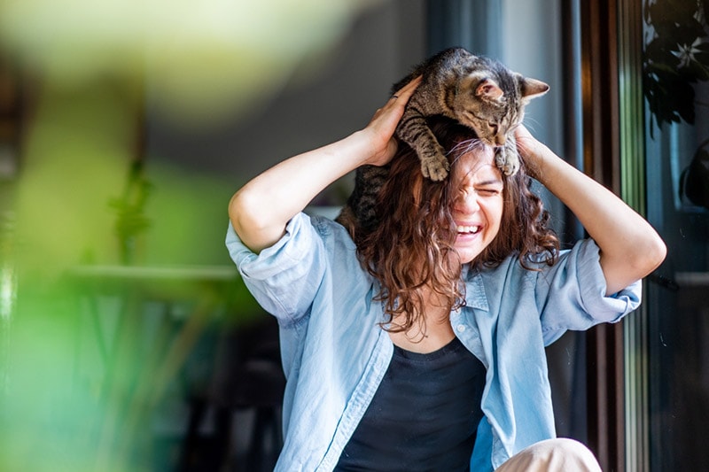 een vrouw die vrolijk lacht met een kat op haar hoofd